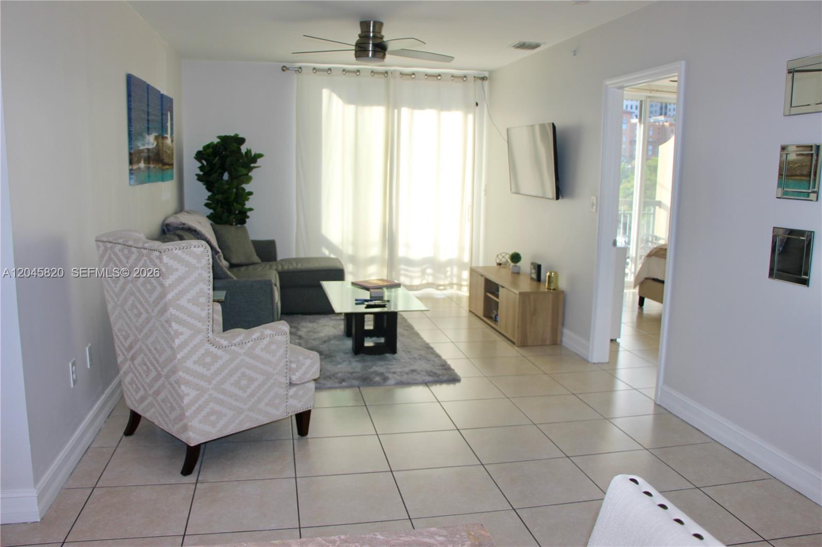 A living room features tile flooring, a gray sectional sofa, an armchair, and a television — 2501 Douglas Rd # 304, Miami FL 33133, MIAMI, FL