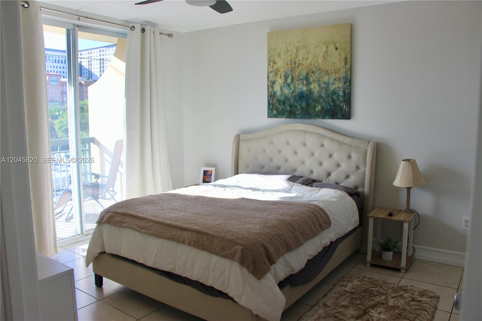 A bedroom features a tufted headboard, a bed with a brown throw, and a balcony view — 2501 Douglas Rd # 304, Miami FL 33133, MIAMI, FL