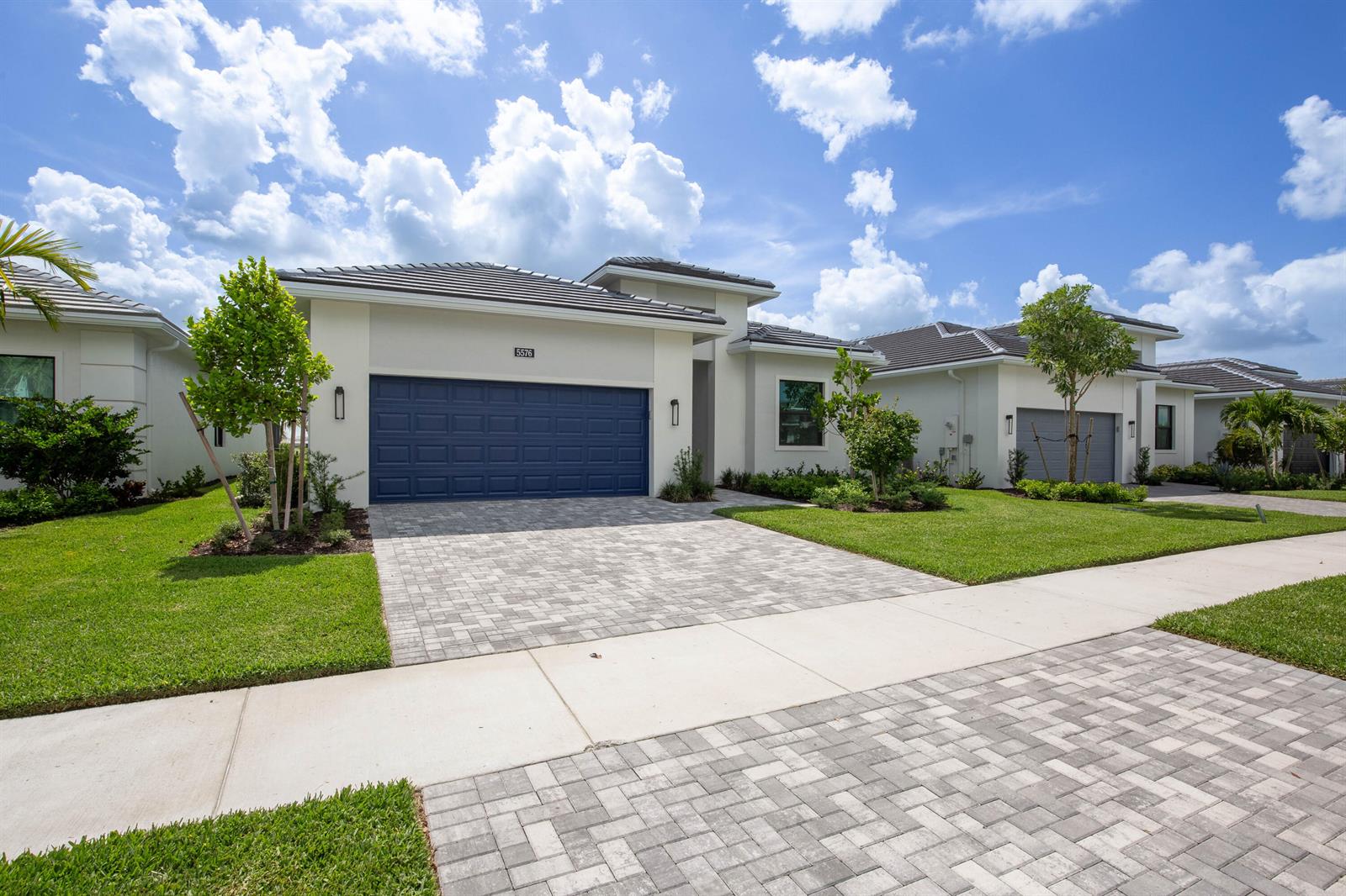 A modern single-story house features a blue garage door, paved driveway, and landscaped front yard — 5576 Captiva Lane, FL 33470, FL