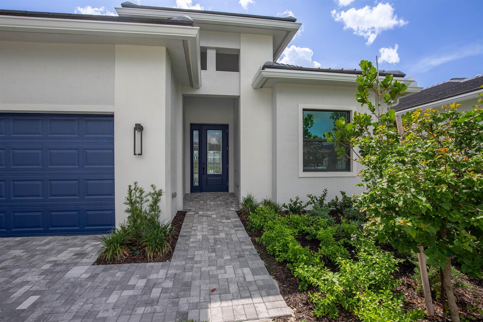 A modern white house exterior features a blue garage door, front door, and paver walkway — 5576 Captiva Lane, FL 33470, FL