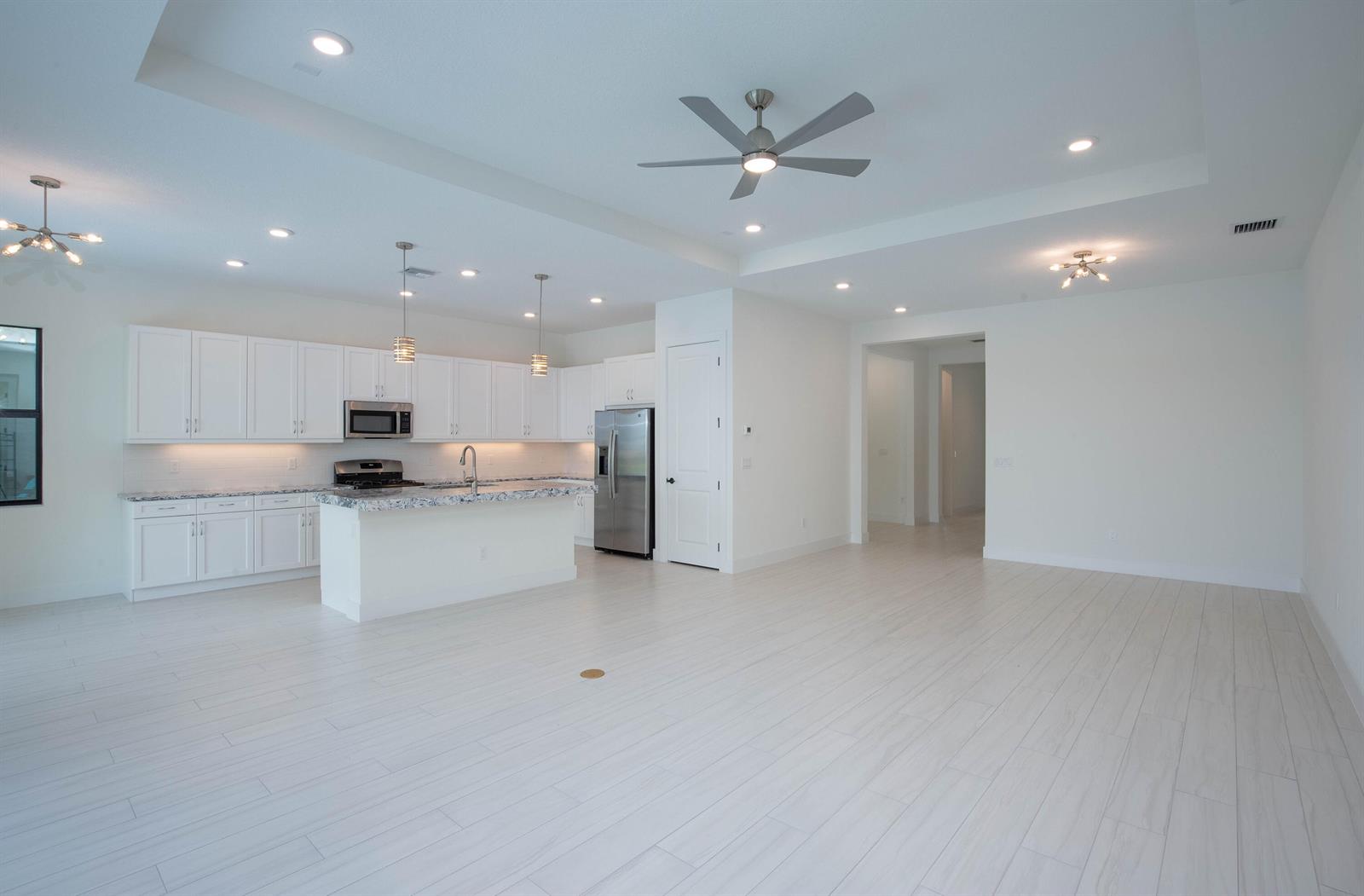 A bright, open-concept kitchen features white cabinetry, granite countertops, and light-colored tile flooring — 5576 Captiva Lane, FL 33470, FL