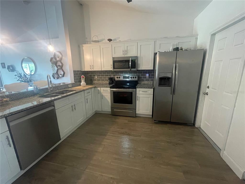 A kitchen with white cabinets, stainless steel appliances, gray tile backsplash, and wood-look flooring — 6714 ANDREA JANE LANE, ORLANDO, FL
