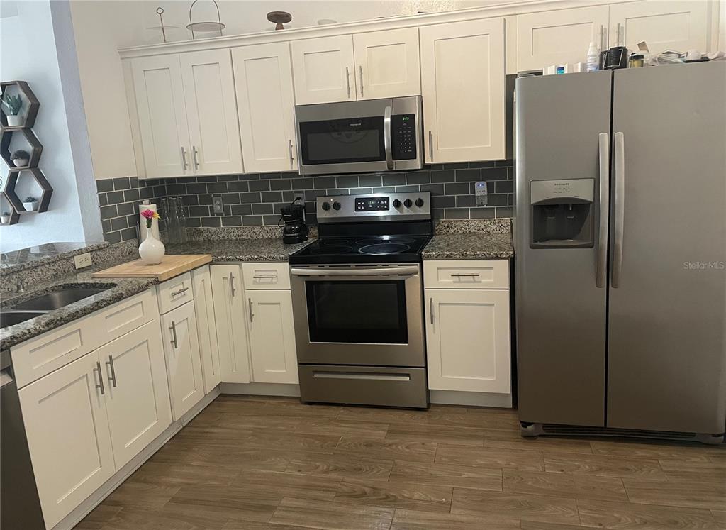 A kitchen features white cabinets, stainless steel appliances, granite countertops, and a gray subway tile backsplash — 6714 ANDREA JANE LANE, ORLANDO, FL