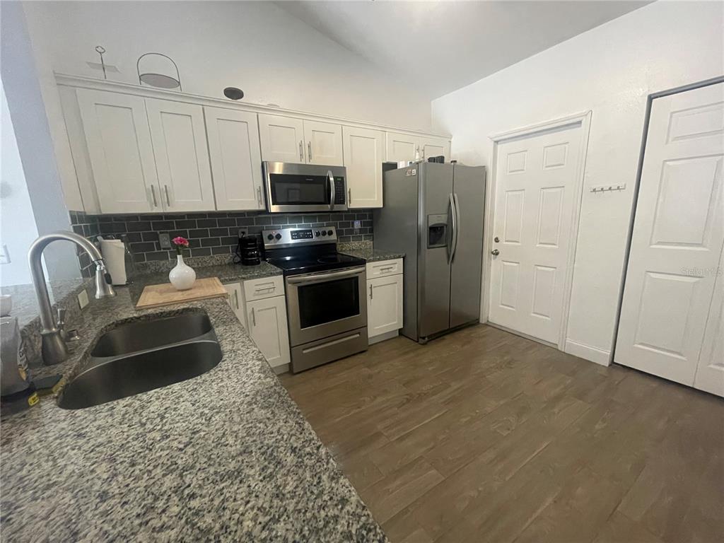 A kitchen features white cabinets, stainless steel appliances, granite countertops, and a gray tiled backsplash — 6714 ANDREA JANE LANE, ORLANDO, FL