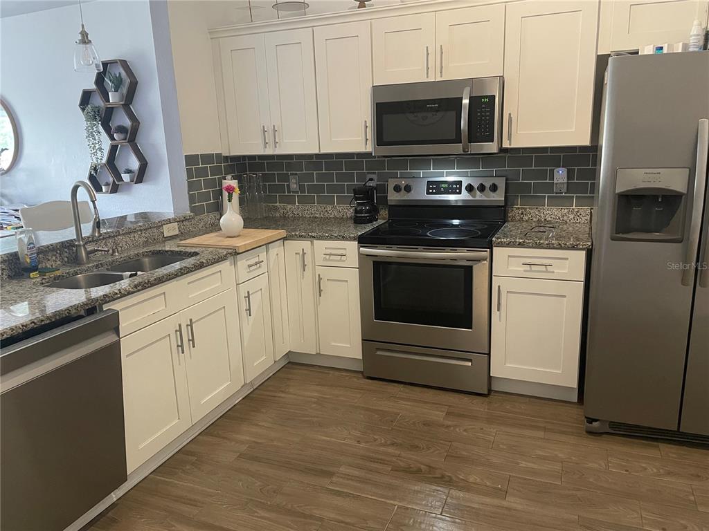 A kitchen features white cabinets, stainless steel appliances, gray subway tile backsplash, and granite countertops — 6714 ANDREA JANE LANE, ORLANDO, FL
