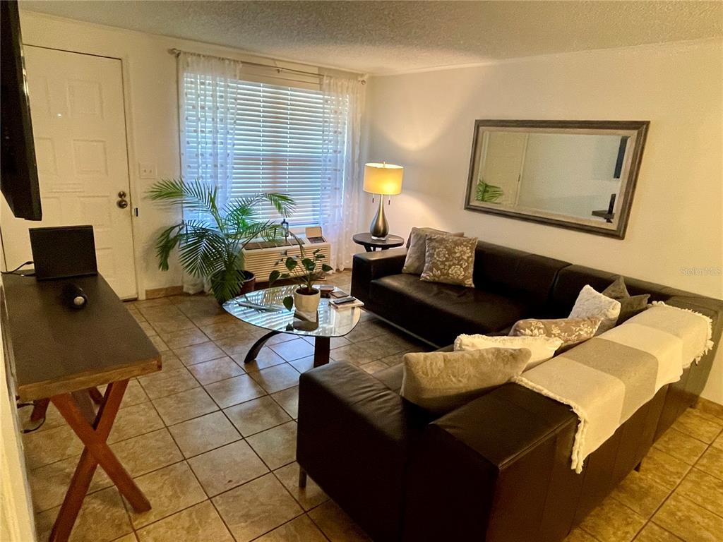 A living room features a dark sectional sofa, a glass coffee table, and tile flooring — 2490 SW 14TH DR UNIT 29, GAINESVILLE, FL