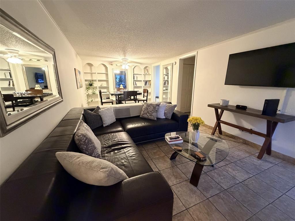 A living room features a large black sectional sofa, a glass coffee table, and tile flooring — 2490 SW 14TH DR UNIT 29, GAINESVILLE, FL