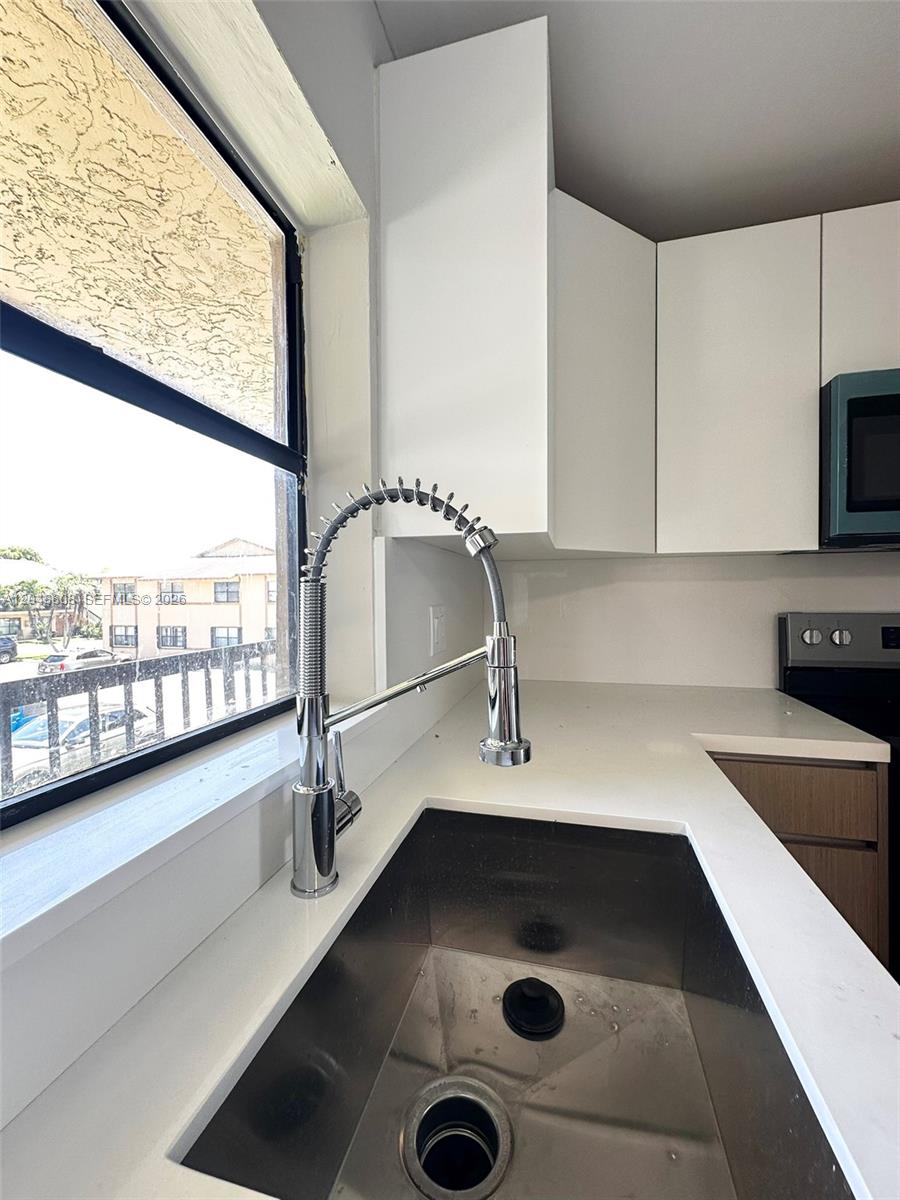A kitchen sink with a chrome faucet sits beneath a window next to white cabinets — 2540 W 67th Pl # 28, Hialeah FL 33016, HIALEAH, FL