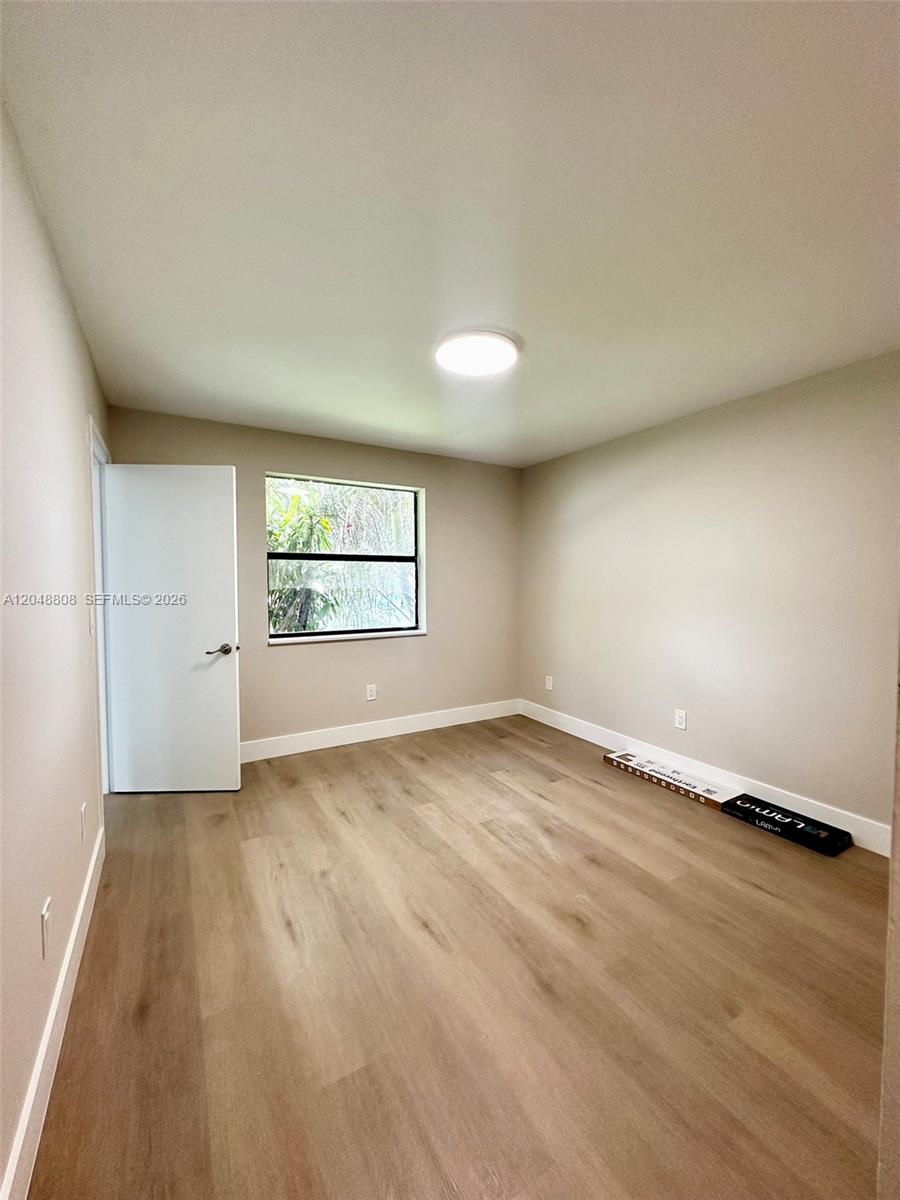 An empty bedroom features light-colored walls, wood-look flooring, a window, and a closed door — 2540 W 67th Pl # 28, Hialeah FL 33016, HIALEAH, FL