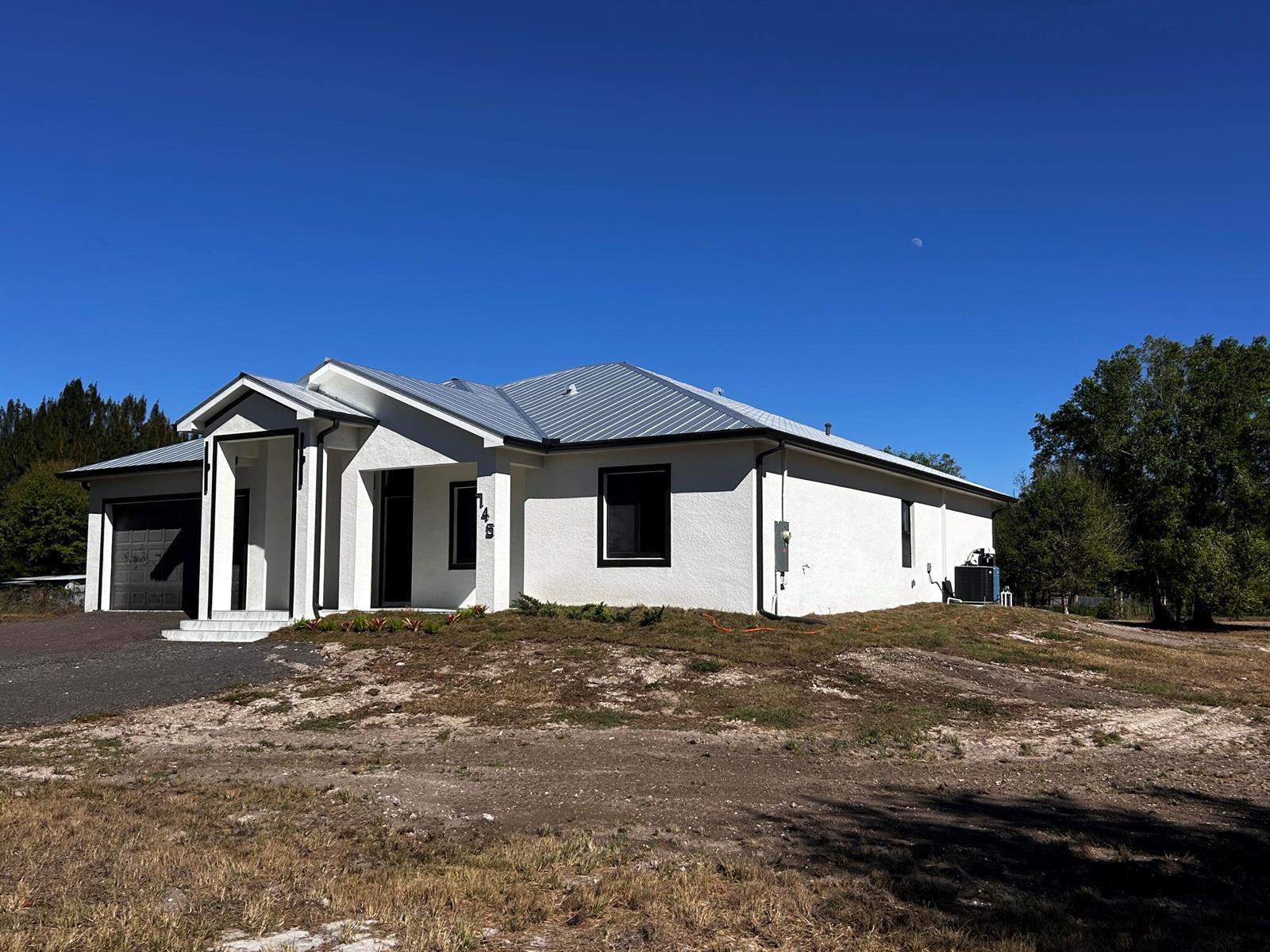 A modern white stucco house with a metal roof and black trim under a blue sky — 745 N Estribo Street, Clewiston FL 33440, CLEWISTON, FL