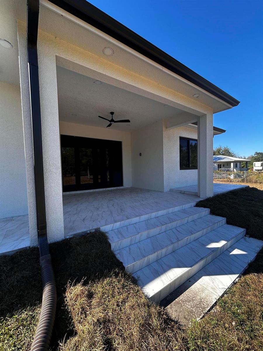 A covered patio with tiled steps leads to a house with a ceiling fan — 745 N Estribo Street, Clewiston FL 33440, CLEWISTON, FL