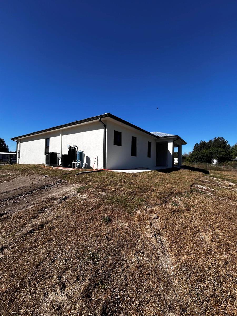 The exterior of a white, single-story house features a water treatment system and HVAC unit — 745 N Estribo Street, Clewiston FL 33440, CLEWISTON, FL