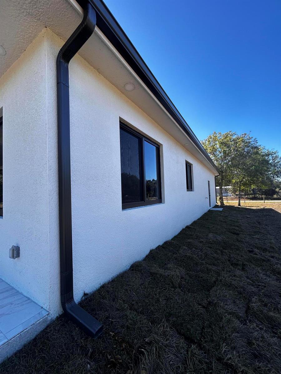 A side view of a white stucco house with black gutters and window frames — 745 N Estribo Street, Clewiston FL 33440, CLEWISTON, FL