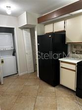 A kitchen features a stacked washer and dryer, a black refrigerator, and tile flooring — 3100 S SEMORAN BOULEVARD UNIT 11, ORLANDO, FL
