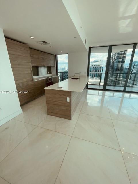 A modern kitchen features wood-toned cabinetry, a central island, and floor-to-ceiling windows with city views — 1300 S Miami Ave # 4001, Miami FL 33130, MIAMI, FL