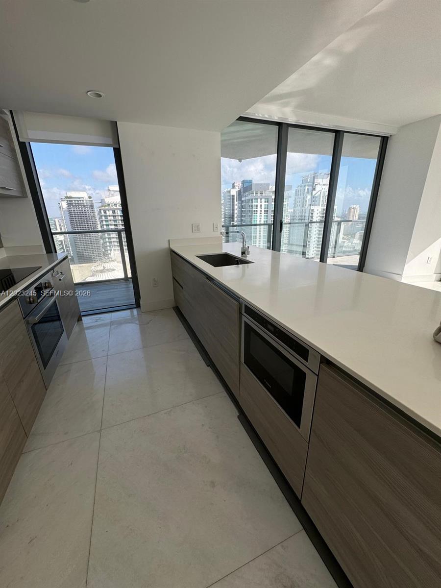 A modern kitchen features light wood cabinetry, white countertops, and floor-to-ceiling windows with city views — 1300 S Miami Ave # 4001, Miami FL 33130, MIAMI, FL