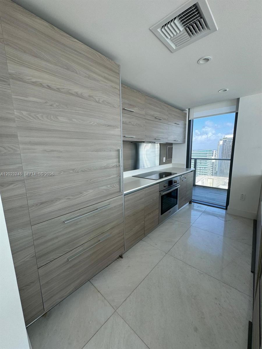A modern kitchen features wood-grain cabinetry, stainless steel appliances, and large white floor tiles — 1300 S Miami Ave # 4001, Miami FL 33130, MIAMI, FL