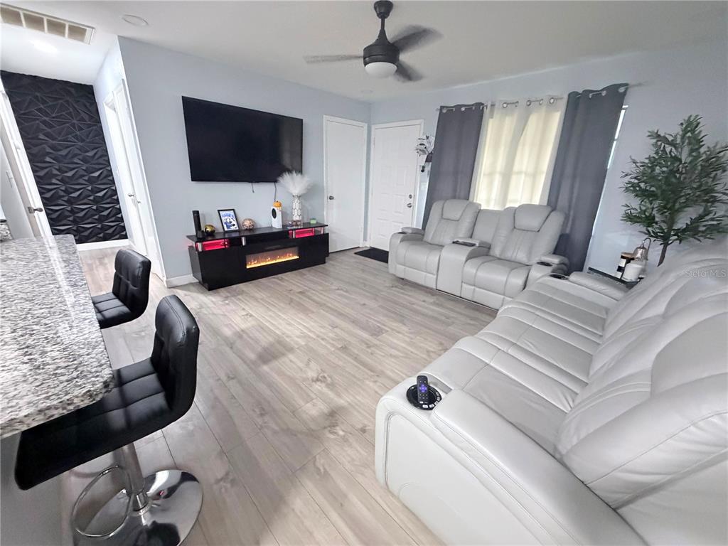 A living room features light wood flooring, a wall-mounted television, and white leather seating — 7281 SE 120TH STREET UNIT 1, BELLEVIEW, FL