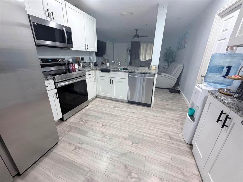 A kitchen features white cabinets, stainless steel appliances, granite countertops, and light wood-look flooring — 7281 SE 120TH STREET UNIT 1, BELLEVIEW, FL
