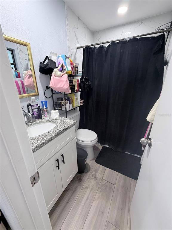 A bathroom features a vanity with a granite countertop, a toilet, and a black shower curtain — 7281 SE 120TH STREET UNIT 1, BELLEVIEW, FL