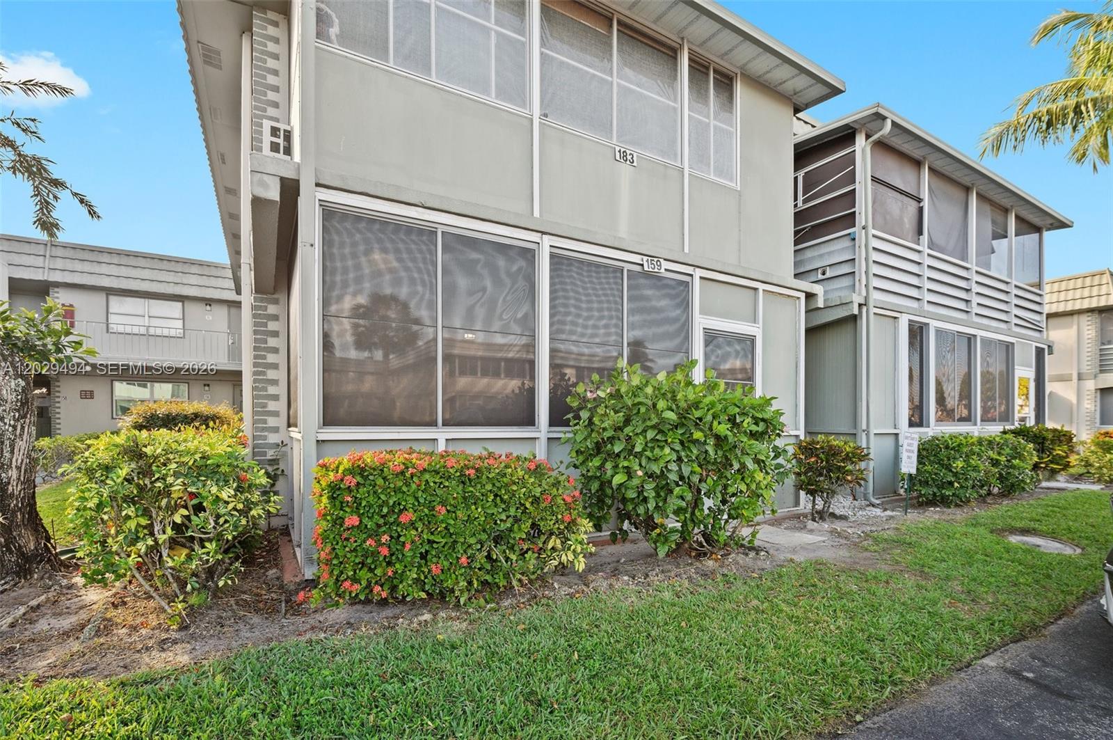 A two-story residential building features screened-in porches, gray siding, and landscaped bushes in front — 159 Brittany D # 159, Delray Beach FL 33446, DELRAY BEACH, FL
