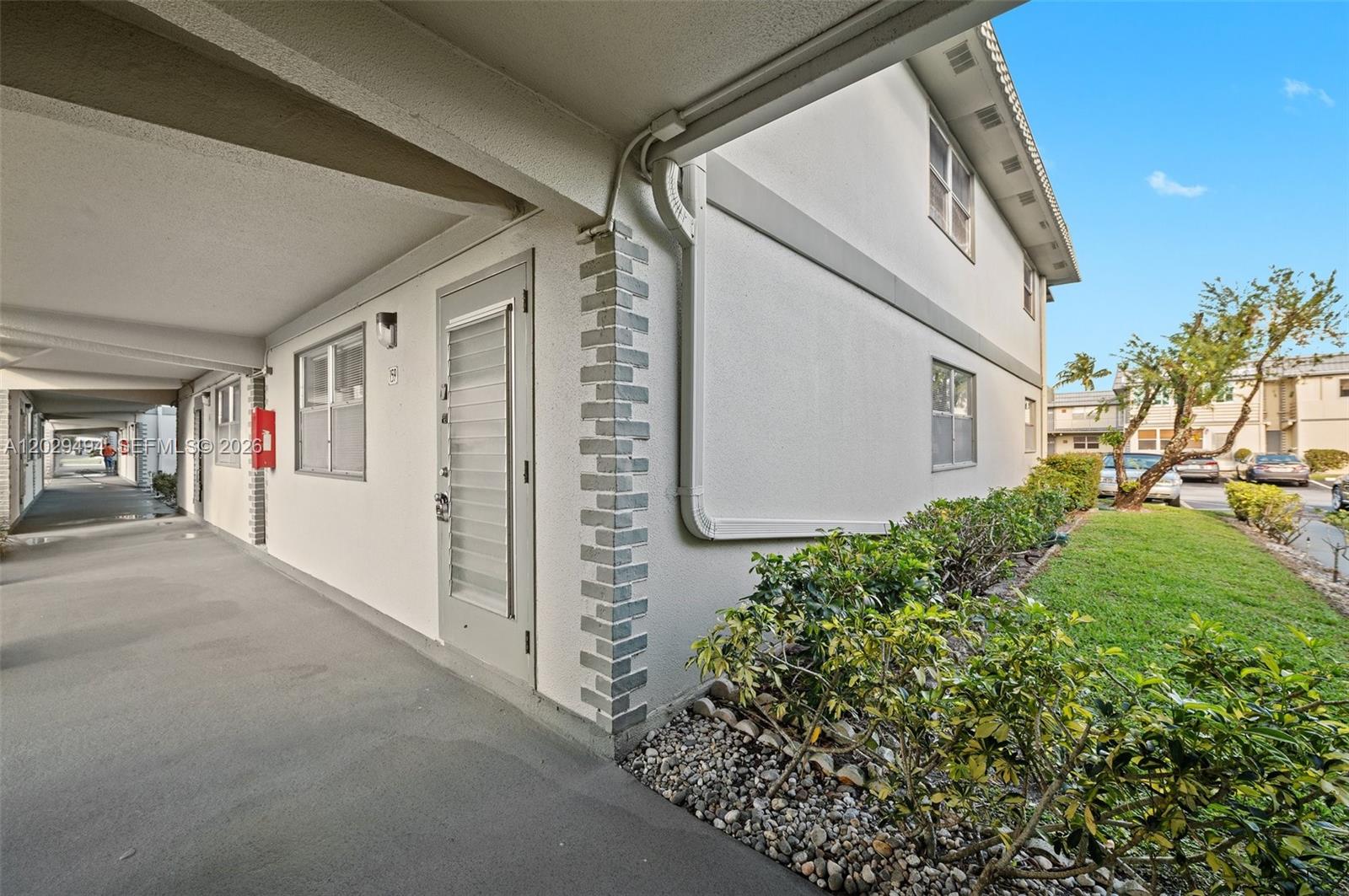 An exterior view shows a covered walkway leading past a building with a white door — 159 Brittany D # 159, Delray Beach FL 33446, DELRAY BEACH, FL
