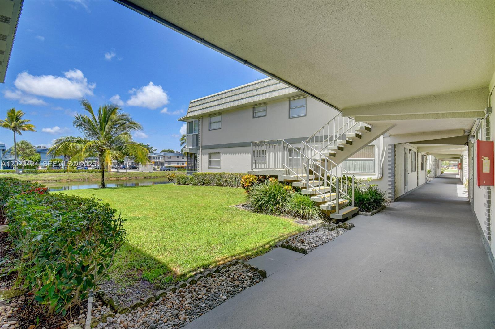 An outdoor walkway leads past a grassy lawn, a small pond, and a staircase — 159 Brittany D # 159, Delray Beach FL 33446, DELRAY BEACH, FL