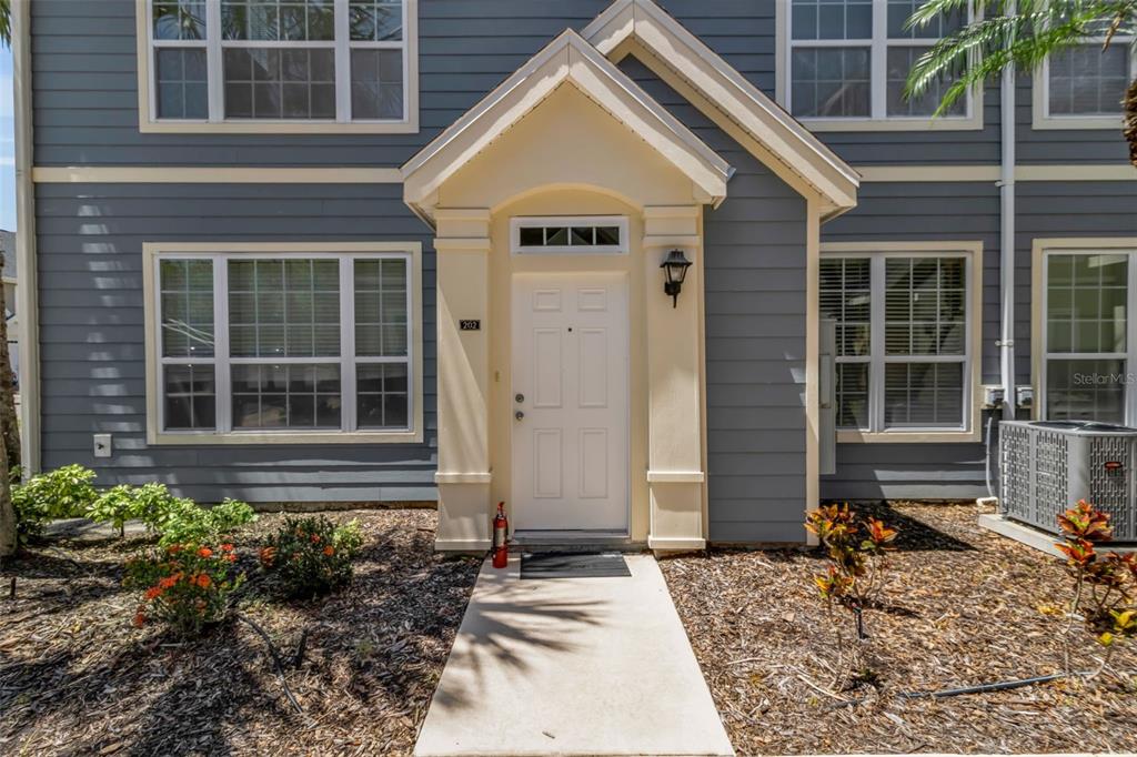 The exterior of a two-story residential building features gray siding, a white door, and landscaping — 5541 ROSEHILL ROAD UNIT 202, SARASOTA, FL