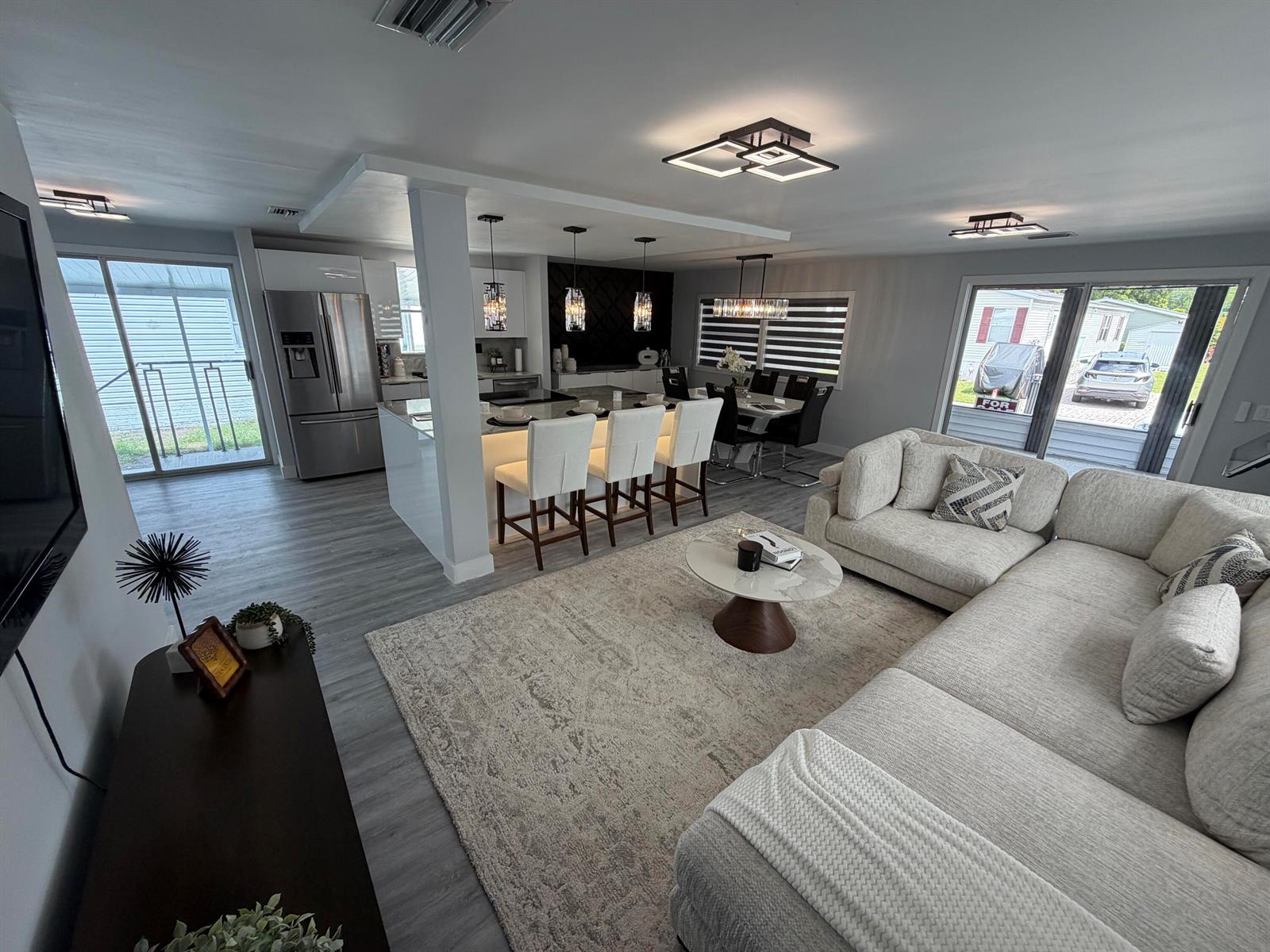 An open-concept living room and kitchen featuring a large sectional, island seating, and modern lighting — 6600 NW 29th Court, Margate FL 33063, MARGATE, FL