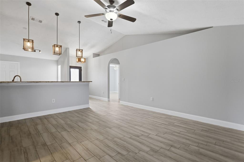A living area with wood-look tile flooring, a vaulted ceiling, and a kitchen breakfast bar — 2943 CIALELLA PASS, ST CLOUD, FL