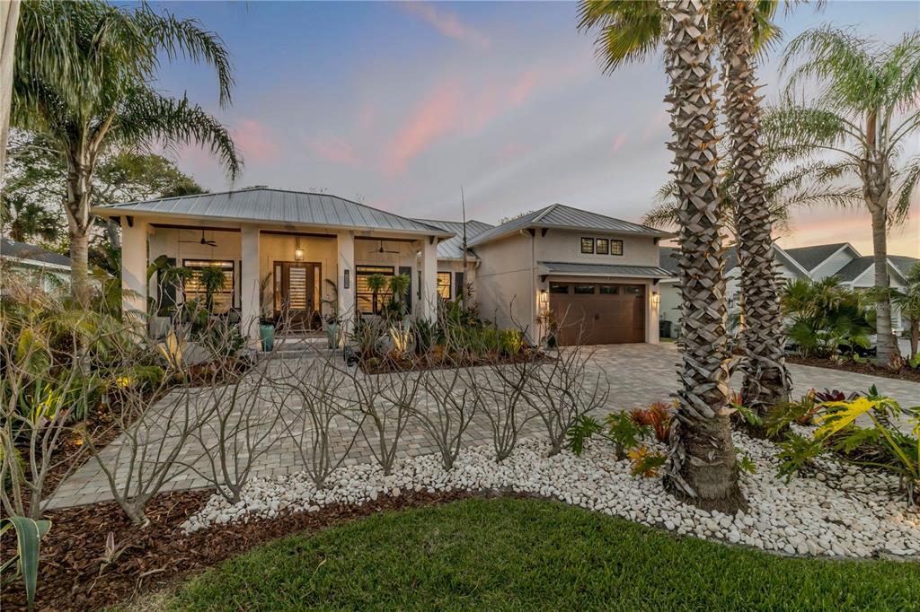 A covered front porch features a wood-paneled ceiling, stone steps, and lush tropical landscaping — 1502 SAXON DRIVE, NEW SMYRNA BEACH, FL