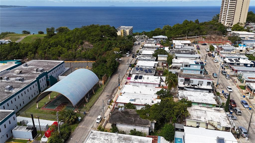 An aerial view shows a residential neighborhood with a covered basketball court near the ocean — 7 CALLE OPALO, AGUADILLA, PR