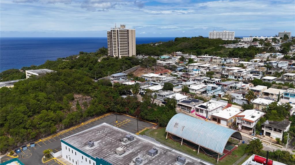 An aerial view shows a coastal neighborhood with a tall apartment building and residential houses — 7 CALLE OPALO, AGUADILLA, PR