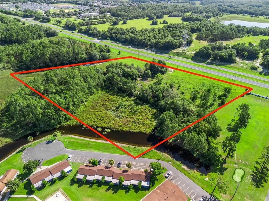 An aerial view shows a vacant, wooded lot outlined in red next to a parking lot — US HIGHWAY 27, LEESBURG, FL