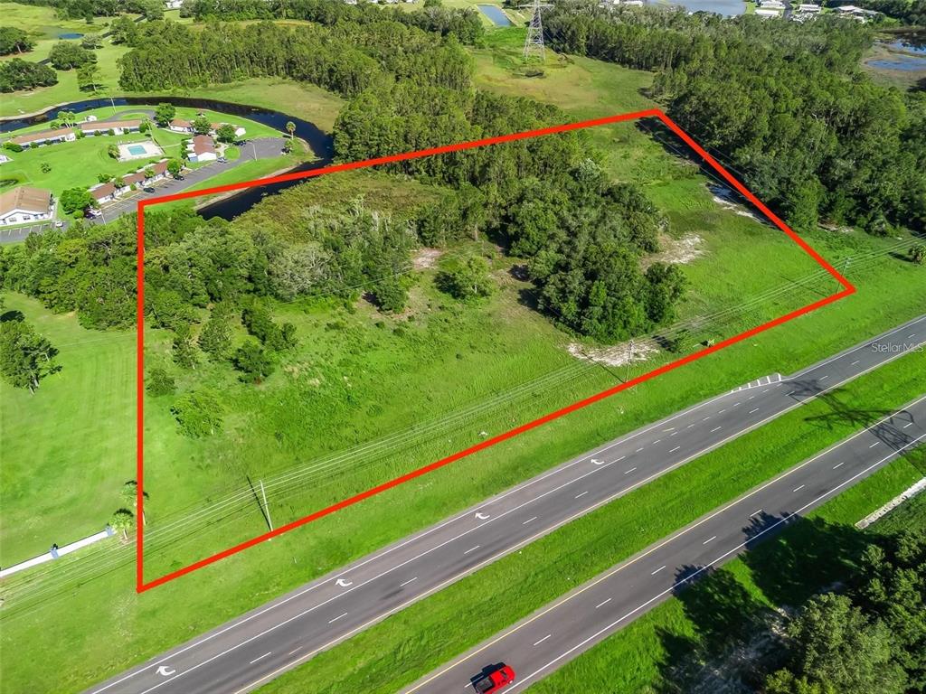 An aerial view shows a vacant, rectangular plot of land bordered by a highway — US HIGHWAY 27, LEESBURG, FL