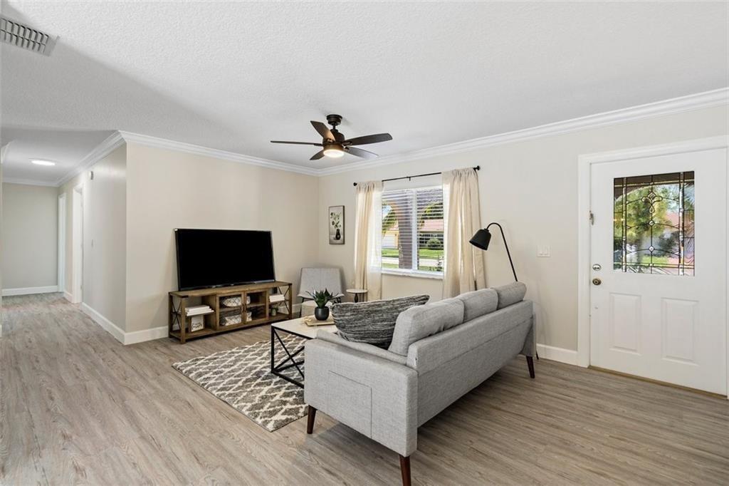 A living room features light wood-look flooring, a gray sofa, and a television on a stand — 10884 Gantry Street, Boca Raton FL 33428, BOCA RATON, FL