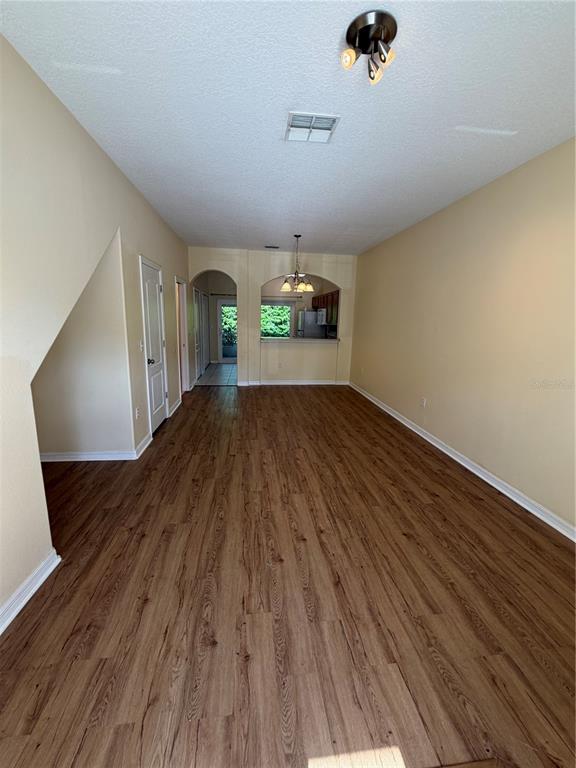 A living area with wood-look flooring, beige walls, and an arched opening to the kitchen — 4154 WINDING VINE DRIVE, LAKELAND, FL