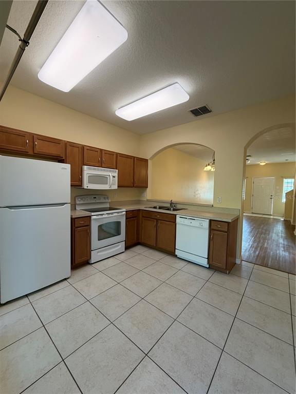 A kitchen with wood cabinets, white appliances, and tile flooring features an arched wall opening — 4154 WINDING VINE DRIVE, LAKELAND, FL