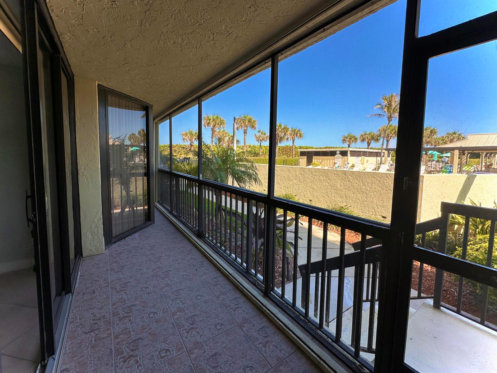 A screened-in balcony with tiled flooring overlooks a swimming pool area and palm trees — 9500 S Ocean Drive # 108, Jensen Beach FL 34957, JENSEN BEACH, FL