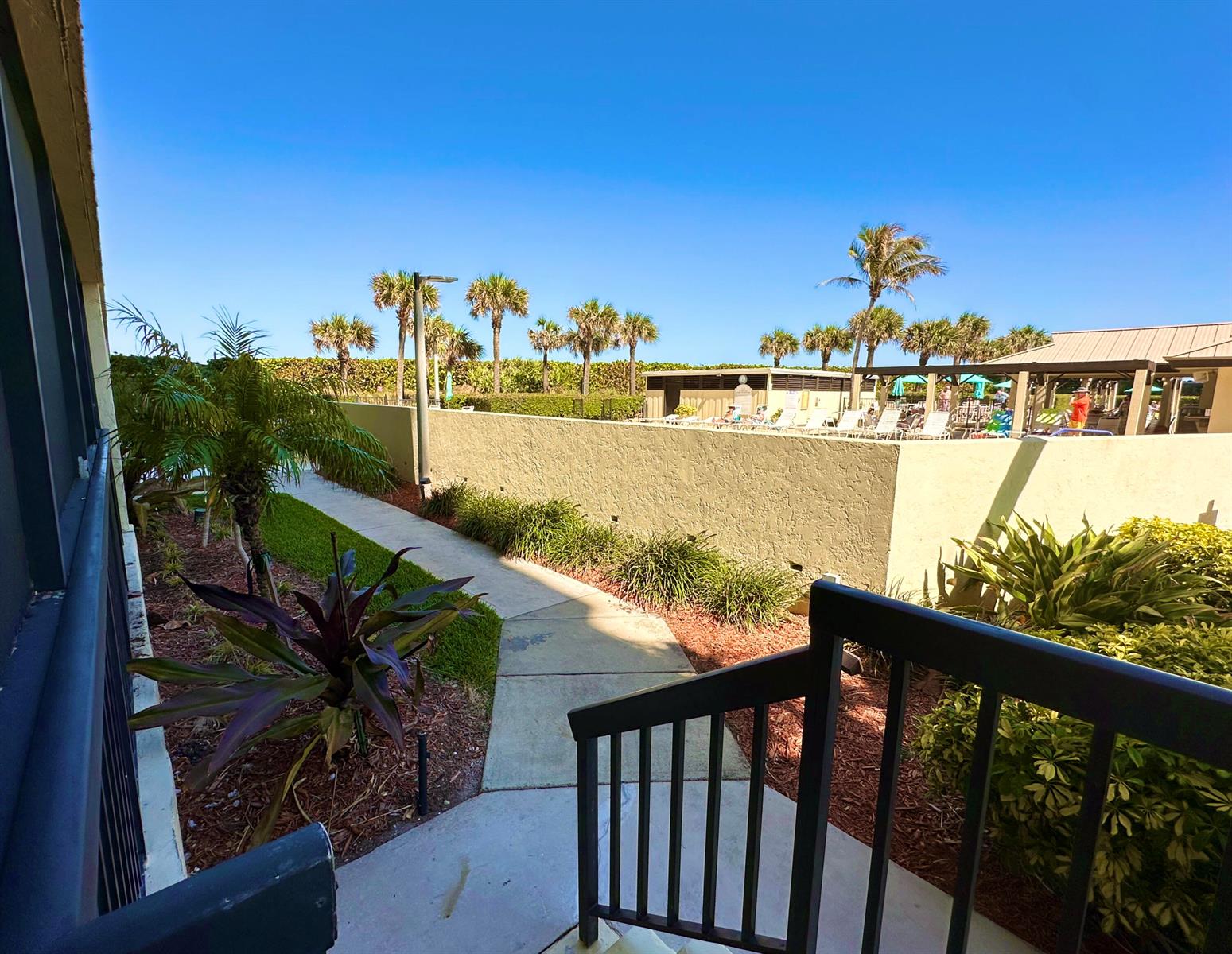 A concrete walkway leads past landscaping toward a pool area with palm trees and fencing — 9500 S Ocean Drive # 108, Jensen Beach FL 34957, JENSEN BEACH, FL