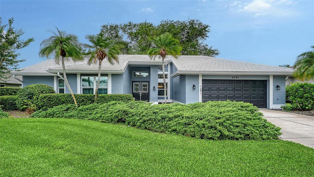 A single-story house with a blue exterior, a tiled roof, and a manicured front lawn — 4391 MAPLEWOOD LANE, SARASOTA, FL