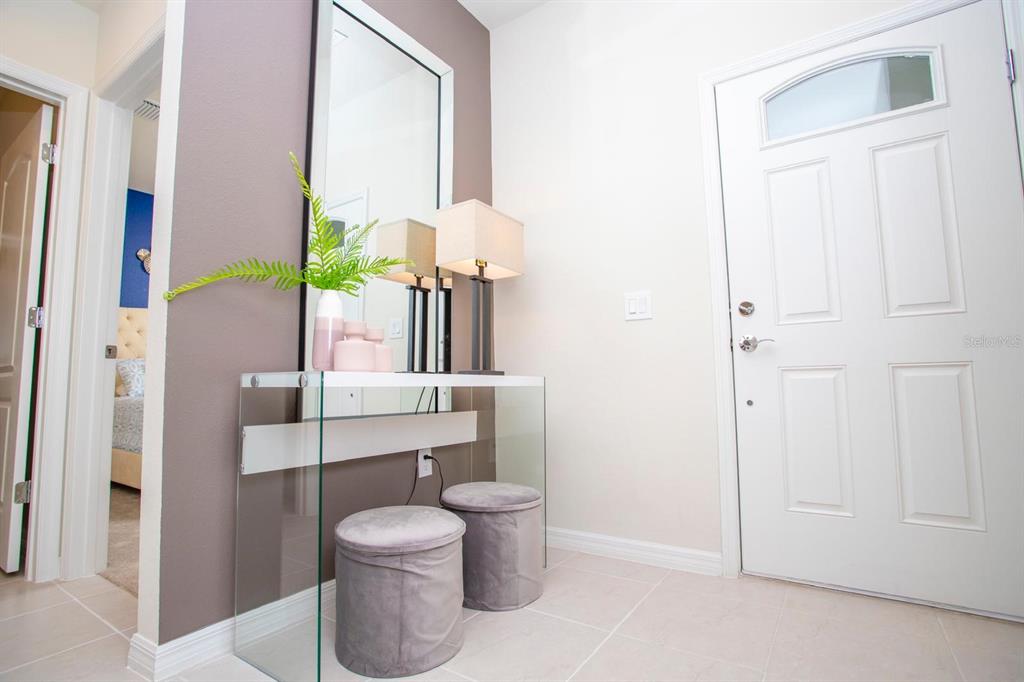 A glass console table with two grey ottomans sits in a foyer with a mirror — 8944 SYDNEY AVENUE, KISSIMMEE, FL