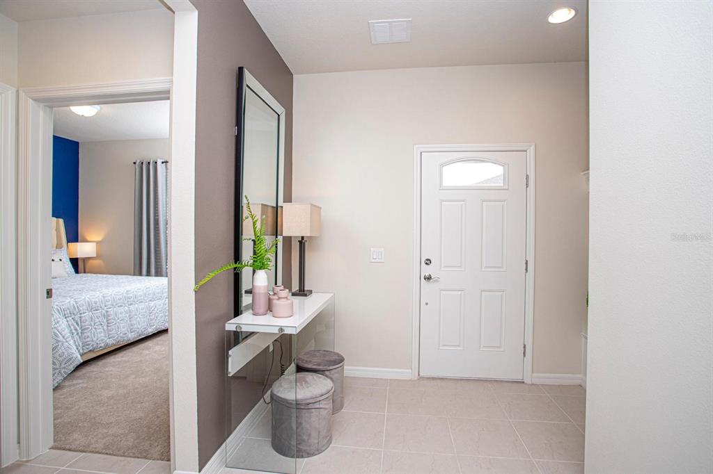 A bright entryway features a white front door, a glass console table, and a bedroom view — 8944 SYDNEY AVENUE, KISSIMMEE, FL