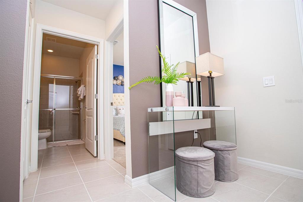A hallway features a glass console table, two grey ottomans, and a mirror against a wall — 8944 SYDNEY AVENUE, KISSIMMEE, FL