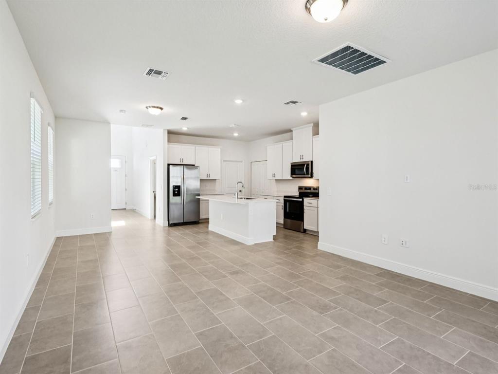 An open-concept kitchen and living area featuring white cabinets, stainless steel appliances, and tile flooring — 2198 WILDBERRY WAY, MINNEOLA, FL