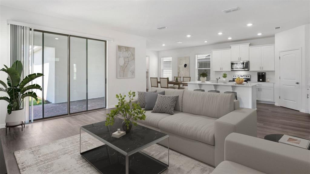 A bright open-concept living room and kitchen featuring white cabinetry, wood-look flooring, and sliding doors — 16834 HOBE SOUND COURT, WINTER GARDEN, FL