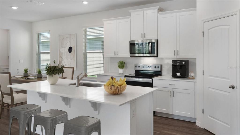 A modern white kitchen features a central island with bar seating and stainless steel appliances — 16834 HOBE SOUND COURT, WINTER GARDEN, FL