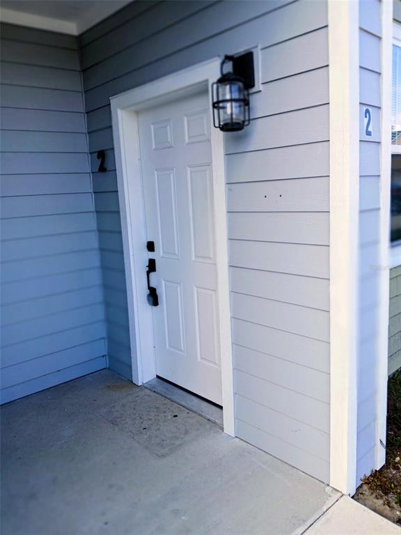 A white front door with a black light fixture is set into light blue siding — 1583 NW 29TH ROAD UNIT 2, GAINESVILLE, FL