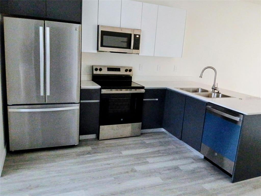 A modern kitchen features stainless steel appliances, dark lower cabinets, white upper cabinets, and countertops — 1583 NW 29TH ROAD UNIT 2, GAINESVILLE, FL