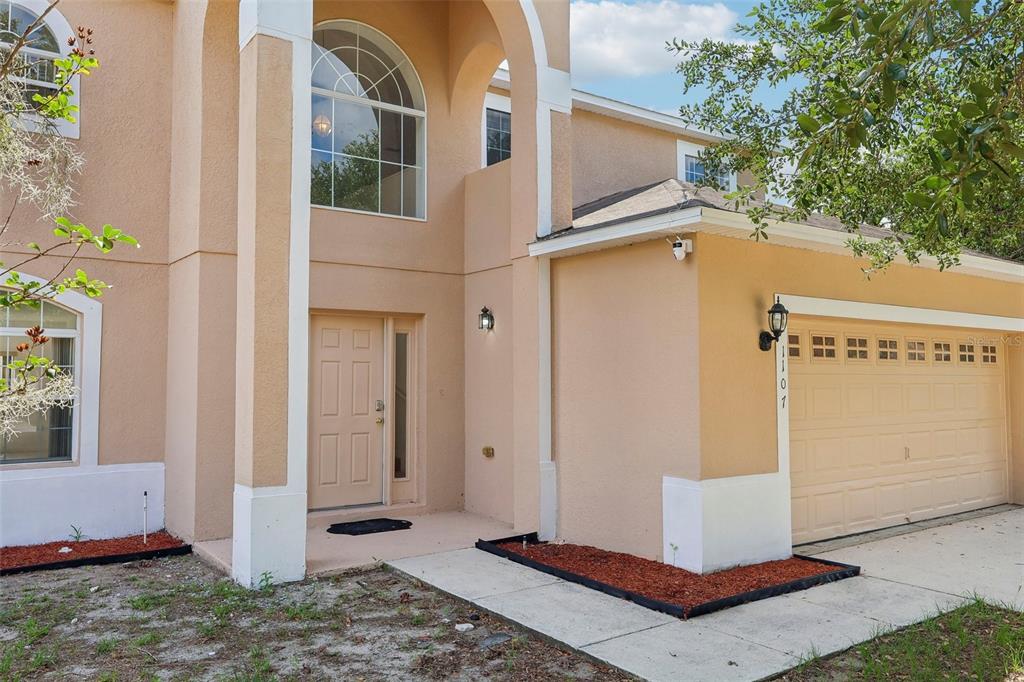 A two-story house exterior with a tan stucco facade, arched entryway, and attached two-car garage — 1107 JAMES WAY, POINCIANA, FL